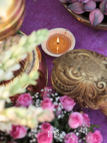 A beautifully detailed shot of a candle in a seashell, surrounded by pink roses and ornate brass objects. Every element is chosen to contribute to the overall theme.