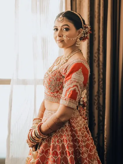 A beautiful three-quarter portrait of the bride, showcasing her stunning red and gold lehenga and intricate jewelry.
