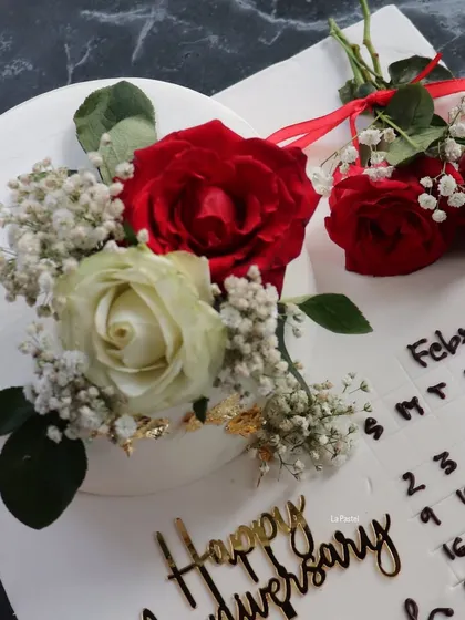 A close-up of the anniversary calendar cake, showing the detail of the hand-piped dates and the beautiful fresh red and white roses.