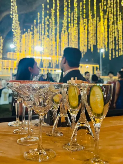 A row of elegant glasses, garnished and ready for service, with the soft glow of event lighting in the background. This shot highlights our preparation and readiness to serve guests with beautifully presented drinks.