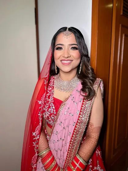 Prachi's wedding day glow. This look features a soft smokey eye and a delicate pink lip, perfectly complementing her red and pink bridal lehenga.