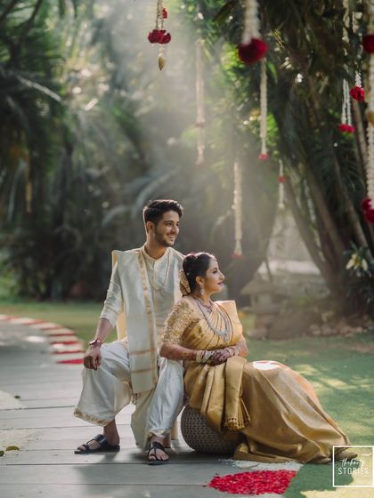 A beautifully composed shot with the couple framed by hanging floral decorations and soft sunlight. This is an example of a perfectly styled heritage pre-wedding photograph.