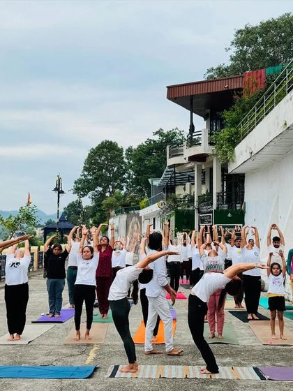 A group of students practices a standing backbend by the water. The serene landscape provides a perfect backdrop for opening the heart.