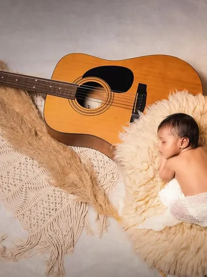 A newborn photoshoot with a musician theme, featuring the baby sleeping peacefully next to a guitar.