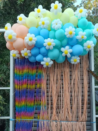 A close-up of a colorful backdrop from a butterfly and floral-themed 4th birthday. The combination of a rainbow tassel wall and a cloud of pastel balloons with daisy accents is perfect for a bright and happy celebration.