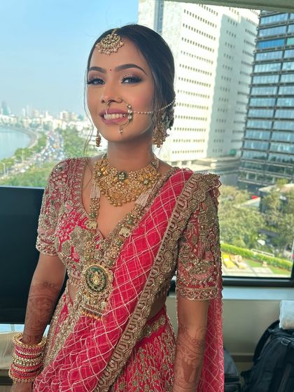 A beautiful bride with a stunning view of Mumbai behind her. Her hair is styled in a classic updo to match her traditional red and gold outfit.