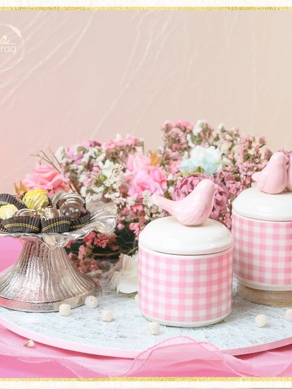 Pretty in pink, this baby girl announcement hamper features gingham jars with sweet bird toppers, a silver platter of chocolates, and a beautiful bouquet of fresh pink flowers.
