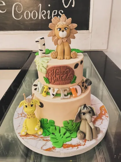 A two-tiered jungle animal cake for a first birthday. This design features a lion, giraffe, and elephant, with a fun mix of animal prints and tropical leaves.