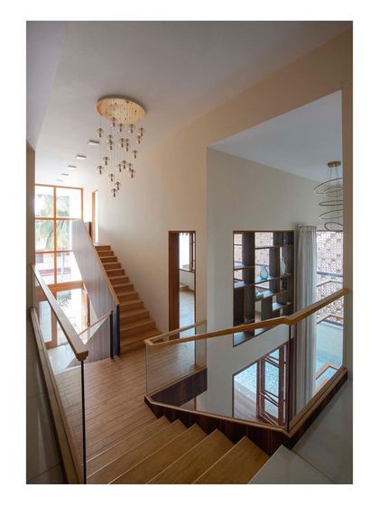 The multi-level staircase in the 'Pool Court House' wraps around the central void, offering constantly changing views of the pool and living areas. The use of wood and glass railings maintains a sense of lightness and transparency throughout the circulation path.