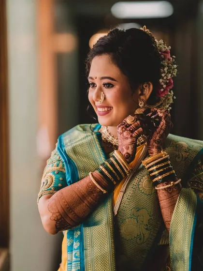 A candid moment of the bride getting ready. The soft, natural light from the window highlights the beautiful texture of her skin and the details of her makeup.