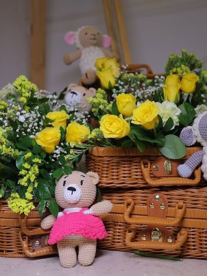 An arrangement of handmade crochet toys and fresh yellow roses in wicker baskets. These details from the Dior-inspired baby shower add a personal, rustic, and charming touch.