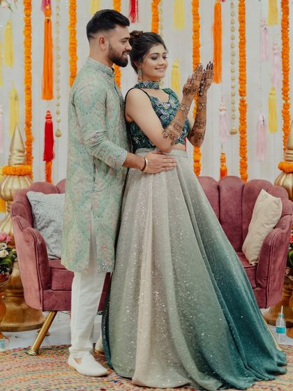 A lovely couple shot from a mehendi ceremony. The bride proudly shows off her henna while standing with her partner.