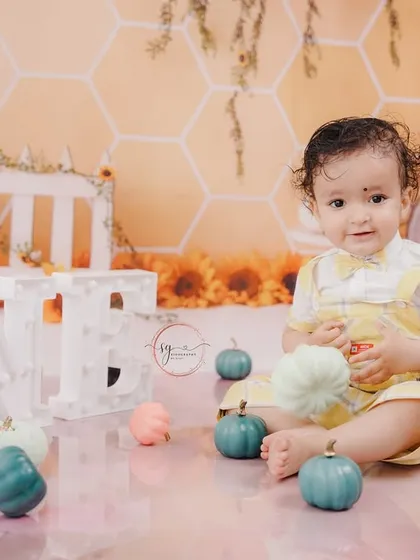 A lovely autumn-themed first birthday shoot, featuring a sunflower and pumpkin backdrop with a warm, sunny color palette.