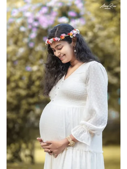 A classic and gentle solo maternity portrait. The mother-to-be, wearing a delicate floral crown, cradles her baby bump with a soft smile, perfectly capturing the quiet joy and anticipation of pregnancy.