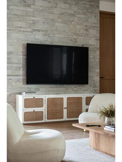This living room embraces a modern farmhouse style with warm wooden textures and rustic stone finish tiles on the TV wall, bringing character and depth to the space.