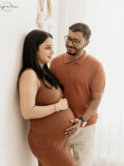 A simple and elegant maternity portrait. The couple stands together against a clean, bright background, their connection being the main focus of the image.