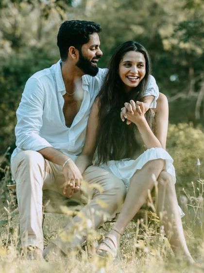 A joyful, sun-drenched photo of the couple sitting in a field. Her bright, happy laugh is the centerpiece of this candid moment.