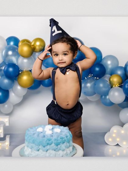 The birthday boy adjusts his party hat while standing next to his cake, ready for the celebration. This is a cute, candid moment from the studio session.