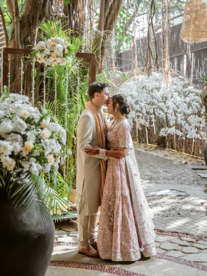 A romantic kiss shared between the couple, framed by lush greenery and beautiful white floral arrangements.