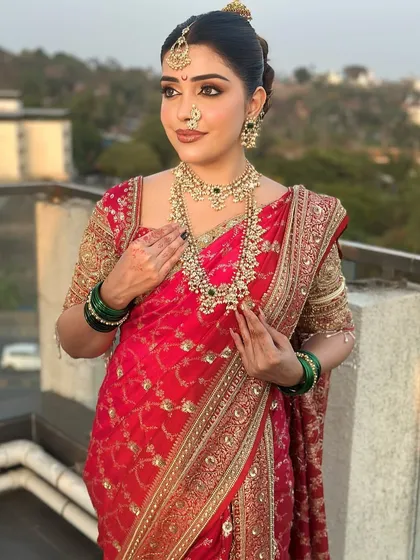 A breathtaking view of a bride against the city skyline. She is wearing a traditional red saree adorned with a layered polki necklace set, combining timeless elegance with a modern backdrop.