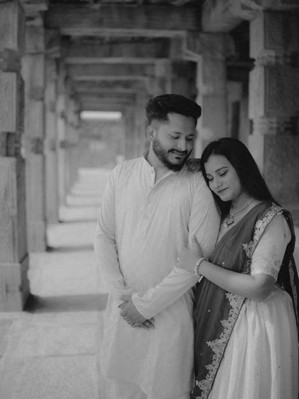 A classic black and white portrait of the couple in a pillared corridor. Using monochrome adds a timeless, artistic feel to this maternity photo, emphasizing emotion over color.
