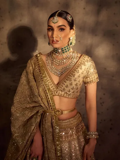 A dramatic and powerful bridal portrait. The makeup is sculpted and defined, with a focus on contour and highlight to complement the gold lehenga and the artistic lighting.