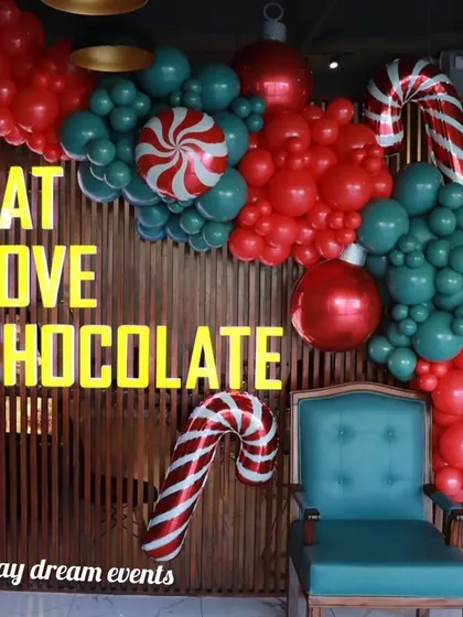 This Christmas selfie corner I designed for a chocolate shop features a fun balloon arrangement with candy cane props against a wooden wall, perfectly matching the 'Eat Love Chocolate' theme.