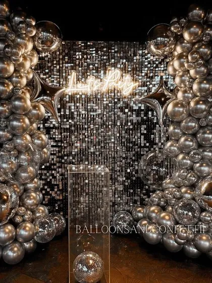 A full shot of another 'Let's Party' setup, this time with a silver sequin wall and matching chrome balloons. The starburst foil balloons and disco balls add that extra sparkle.