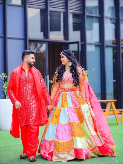 A happy, candid moment of the couple walking hand-in-hand at their Mehendi function. The bride's colorful lehenga and the groom's bright red kurta create a visually stunning pair.