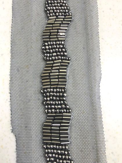 A detailed shot of a wavy, geometric beaded lace. The pattern is formed by arranging metallic bugle beads on a sheer net fabric, perfect for adding texture and shine to necklines or cuffs.