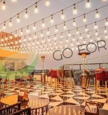 A wide shot of the rooftop at Lord of The Drinks, Agra, at dusk. You can see the entire space lit up with string lights, with our various seating arrangements spread across the floor. This shows the grand scale of the project and the beautiful ambiance our furniture helps create.