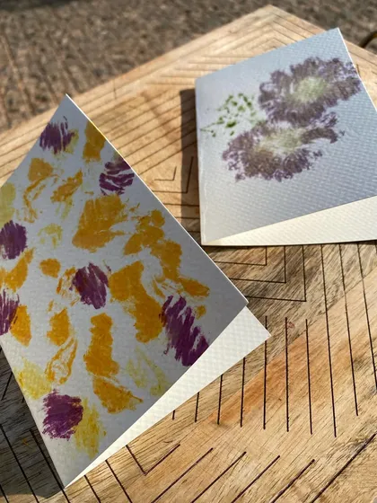 Two finished greeting cards, each with a unique design. One features abstract patterns from petals, while the other showcases the distinct shape of a flower, showing the versatility of the technique.
