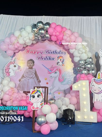 A cute unicorn theme for Vedika's first birthday. The outdoor setup features a pink backdrop with a balloon arch, multiple unicorn cutouts, and a marquee number '1'.