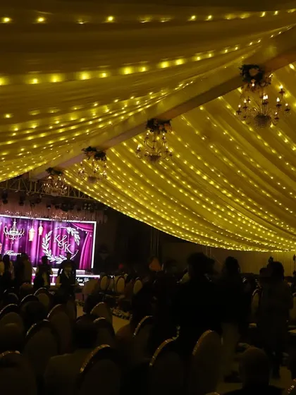 A grand stage setup for a 50th Golden Anniversary celebration. The large LED screen displays the couple's photo, and the ceiling is draped with fabric and fairy lights, creating a golden, celebratory glow.