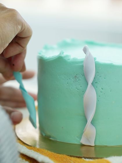 A close-up of a student applying a delicate fondant twist to the side of a cake. This is one of the many modern decorating techniques we teach to add elegance and visual interest.