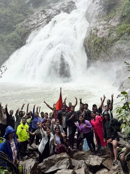Our group celebrating with hands in the air in front of the mighty Dudhsagar falls. The energy and excitement are contagious.