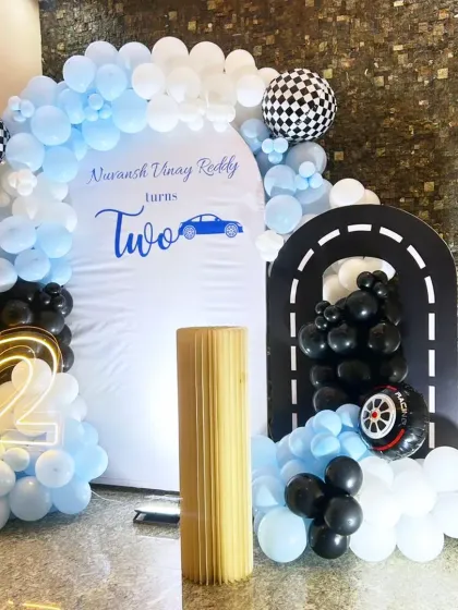 A sleek and modern car-themed second birthday. The "Two Fast" theme is brought to life with a custom white backdrop, a balloon arch in blue, black, and white, and a fun racetrack cutout.