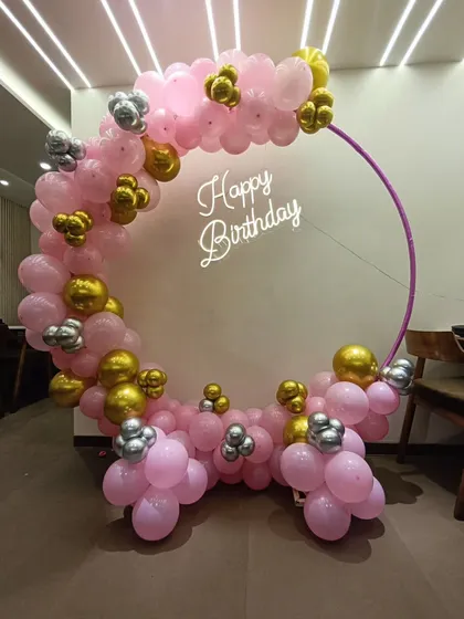A simple yet elegant birthday ring decoration. The hoop is partially decorated with pink, gold, and silver balloons, with a 'Happy Birthday' neon sign floating in the middle.