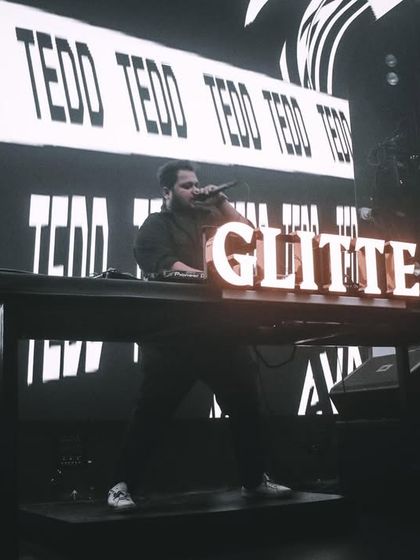 Lights low, beats high. A black and white shot of me on the mic at Glitte, with my name on the console and the big screen.