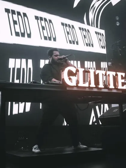 Lights low, beats high. A black and white shot of me on the mic at Glitte, with my name on the console and the big screen.