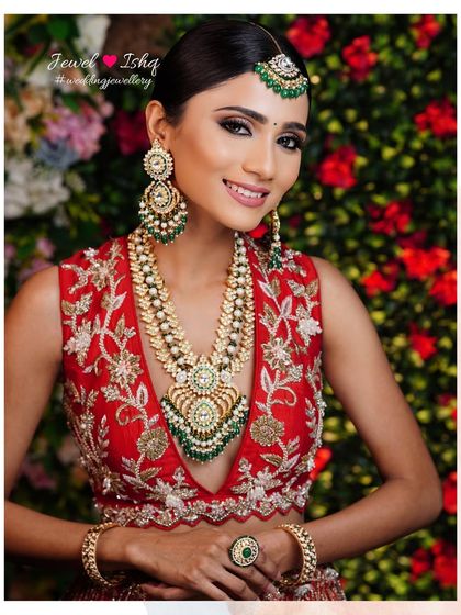 A happy bride showcasing her full look against a floral backdrop. The long, layered necklace is the centerpiece of her stunning ensemble.