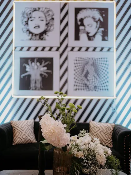A lounge area from the 'Love & Illusion' Sangeet, featuring a black leather sofa against a wall with diagonal stripes and pop-art prints.