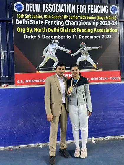 A gold medalist from the senior women's category at the Delhi State Championship, standing proudly with her coach.