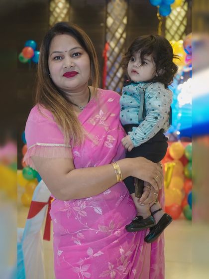 A mother holds her young child, posing for a portrait against a colorful party backdrop.