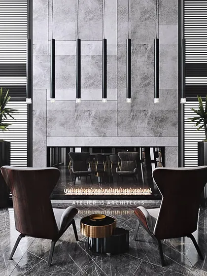 A cozy seating area in front of a grand fireplace set in a grey marble wall. The high-back armchairs create an intimate conversation spot within a larger, double-height space, showcasing our skill in creating different scales of experience.