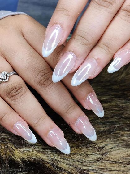 A subtle and chic French manicure with a sheer, pearly base and delicate white tips on long, tapered almond nails.