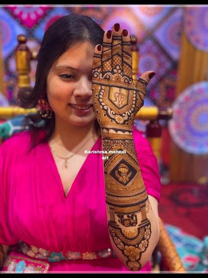A bride showing the detailed mehendi on the back of her hand. The design includes personal initials and symbolic figures, perfectly complementing her wedding look.