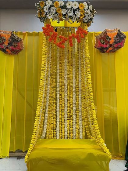 A traditional Haldi seating arrangement with a backdrop of marigold and tuberose strings, accented with colorful Rajasthani umbrellas.
