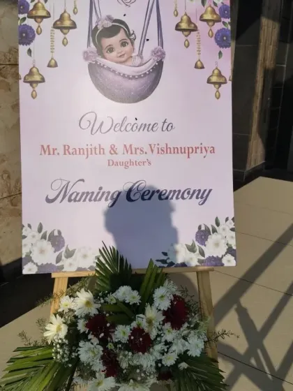 A close-up of a personalized welcome sign for a Naming Ceremony. The sign features a sweet illustration and is adorned with a bouquet of fresh flowers.