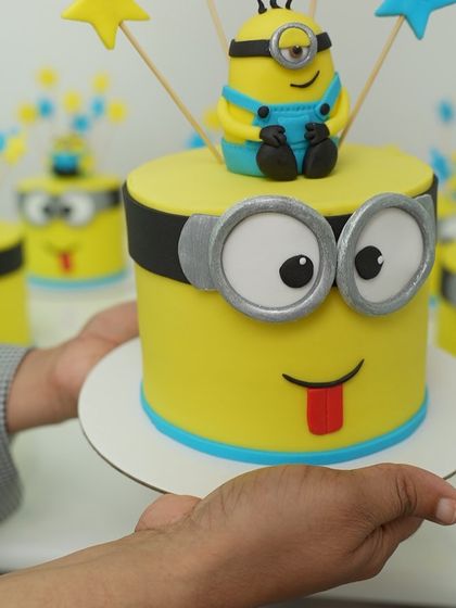 A student proudly holds up their finished Minion cake. This hands-on project teaches everything from covering the cake in fondant to crafting the small details like the goggles and smile.